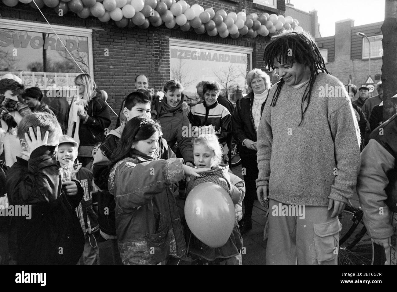 Ouverture de Zegwaard Fitness Haarlem Slachthuisstraat pays-Bas, Whizgle News, Dutch Desk, pays-Bas, 1950 - 2000 le 19-12-1997. Voici les rubriques de l'image. Dans un cadre extérieur animé, un groupe d'enfants se rassemble, leurs visages illuminés d'excitation. Ils sont entourés de décorations de ballons enfilées sur une devanture, ajoutant des touches de couleur à la scène, tandis que l'atmosphère est lumineuse et festive. Au centre de la scène se trouve un adulte, apparemment engagé et joyeux, avec de longs cheveux foncés coiffés de dreadlocks. Son comportement détendu contribue à l'humeur joyeuse. A proximité, une fille avec Banque D'Images