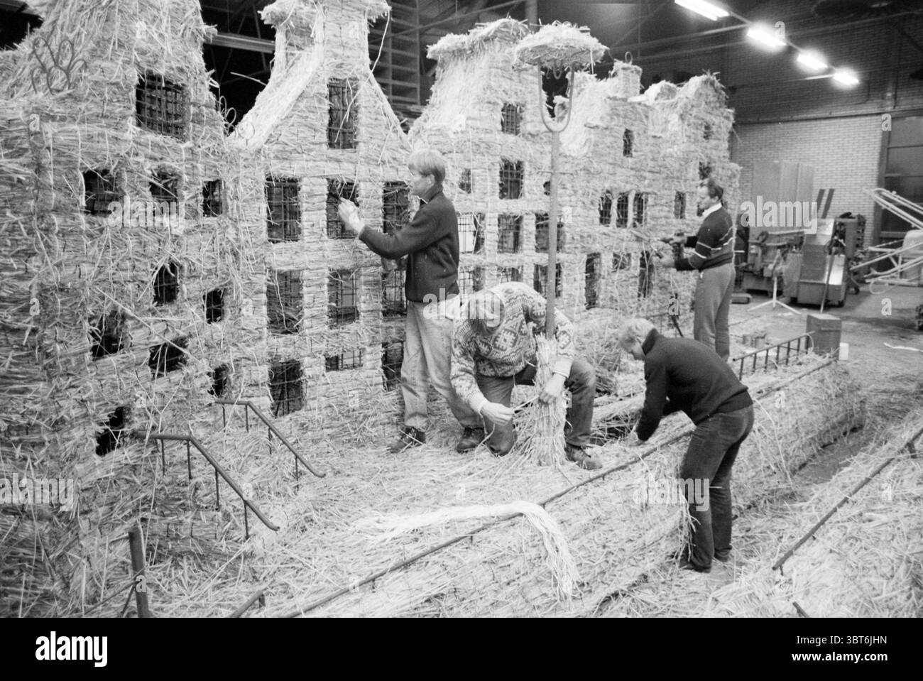 Structure de wagon avec maisons de canal parade de Zilk, Whizgle News, Dutch Desk, pays-Bas, 1950 - 2000 le 12-04-1979. Voici les rubriques de l'image. Dans un grand espace industriel, un groupe d’individus est engagé dans un projet créatif impliquant paille. Le cadre présente le contour squelettique d'une structure qui ressemble à une rangée de vieilles maisons rustiques. Ces maisons sont construites à partir de faisceaux de paille entrelacés avec un certain type de charpente métallique, leur donnant un aspect primitif mais artistique. Les gens sont habillés en vêtements décontractés, certains portant des vestes et d'autres en chandails, Banque D'Images