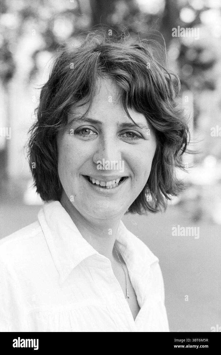Portrait Danielle Kraft. Portraits, Whizgle News, Dutch Desk, pays-Bas, 1950 - 2000 sur 26-07-1979. Ce sont les éléments de l'image. La scène capture une jeune femme avec un sourire chaleureux et invitant. Elle a des cheveux de longueur moyenne et touffus qui encadrent son visage, lui donnant un look détendu et naturel. Sa tenue vestimentaire est une chemise boutonnée de couleur claire, contribuant au sentiment général de fraîcheur et de simplicité. En arrière-plan, une végétation douce et floue suggère un parc ou un cadre extérieur, évoquant un sentiment de tranquillité et d'ouverture. La composition attire le regard sur ses traits expressifs, partic Banque D'Images