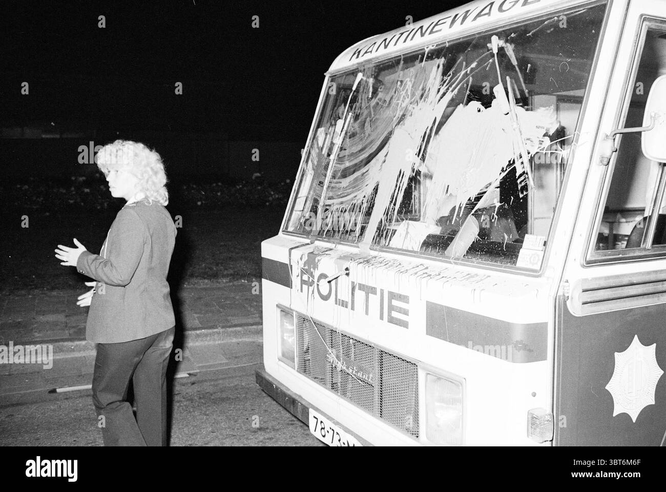 Transport de déchets nucléaires Petten - Velsen transport Companies Petten, Whizgle News, Dutch Desk, pays-Bas, 1950 - 2000 le 01-09-1981. Ce sont les éléments de l'image. La scène représente un cadre nocturne, où une femme est positionnée sur le côté gauche de la composition, son corps légèrement tourné comme si elle s'adressait à quelqu'un ou réfléchissait à la situation. Elle a les cheveux bouclés et blonds et est habillée d'une veste sombre, qui contraste avec les éléments plus lumineux autour d'elle. À sa droite se tient un camion de nourriture, portant des signes visibles de détresse. La surface du chariot est marquée WIT Banque D'Images
