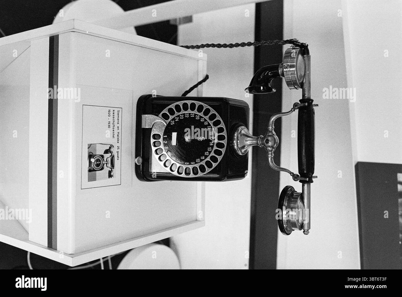 Ancien bureau de réception téléphonique 100 ans de télécommunications PTT Haarlem pays-Bas, Whizgle News, Dutch Desk, pays-Bas, 1950 - 2000 le 01-09-1981. L'image inclut ces rubriques. La scène dispose d'un téléphone vintage, caractérisé par son cadran rotatif classique et un design élégant. Le téléphone est principalement noir, avec un corps élégant qui scintille doucement sous l'éclairage ambiant. Le cadran, avec sa configuration circulaire, présente des numéros disposés dans le sens horaire, chacun clairement défini et contrastant doucement avec la surface sombre. A côté du téléphone, il y a un smal Banque D'Images