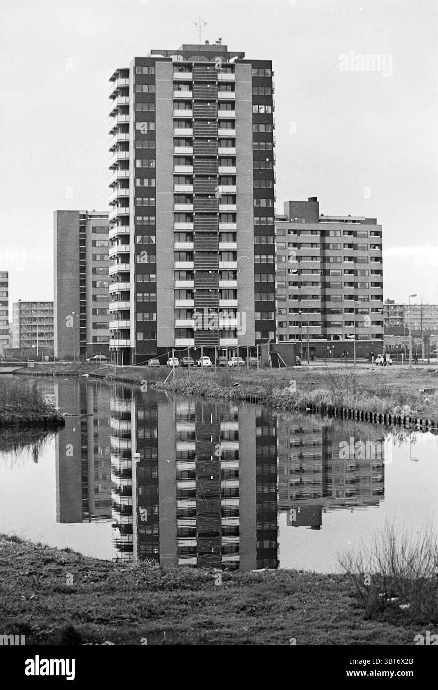 Appartement pour retraités Costa del sol extérieur intérieur, Whizgle News, Dutch Desk, pays-Bas, 1950 - 2000 sur 13-12-1974. Ces rubriques apparaissent dans l'image. La scène présente un groupe de grands bâtiments, principalement composés de béton et de verre, disposés dans une disposition quelque peu symétrique. Au centre de la composition se trouve une structure de grande hauteur moderne et proéminente avec un mélange de panneaux sombres et clairs, des balcons visibles sur plusieurs étages. La façade reflète un motif horizontal, ajoutant à son intérêt architectural. Au premier plan, un plan d'eau calme reflète les bâtiments, créant une symétrie Banque D'Images