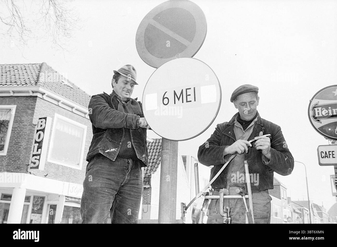 Mise en place de panneaux de signalisation trafic sécurité routière, Whizgle News, Dutch Desk, pays-Bas, 1950 - 2000 le 20-03-1969. L'image inclut ces rubriques. Dans cette scène, deux hommes sont engagés dans une tâche, debout devant un panneau circulaire qui est destiné à transmettre une date. Le signe est bien visible, attirant l'attention en raison de sa simplicité et de sa forme circulaire. Le premier homme, positionné à gauche, a une expression sérieuse car il se concentre intensément sur le signe, portant une veste sombre et une casquette qui ajoute à son apparence robuste. Il semble ajuster ou manipuler la rue du panneau Banque D'Images