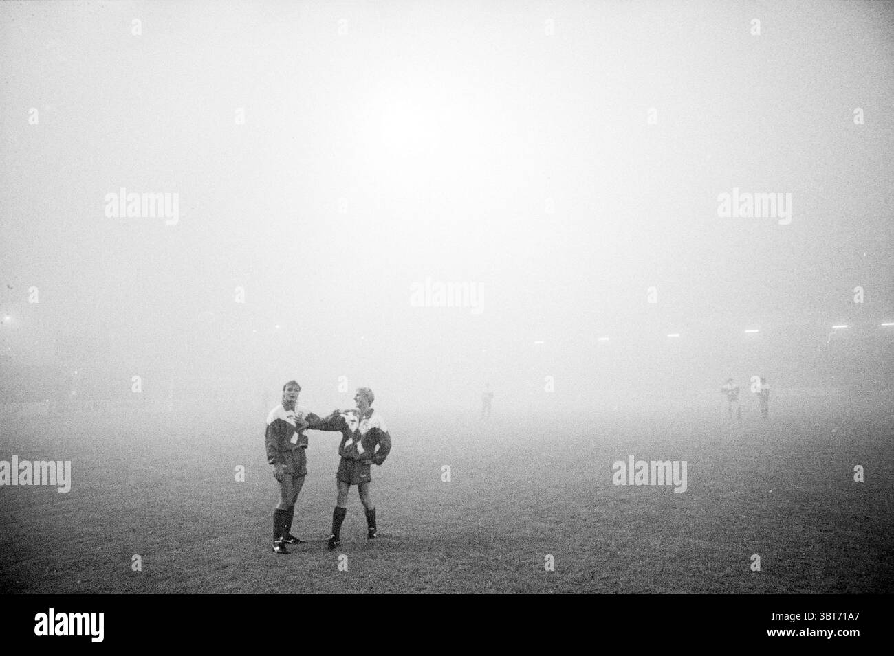Haarlem - de Bosch (AFG), Whizgle News, Dutch Desk, pays-Bas, 1950 - 2000 le 08-10-1991. L'image contient ces rubriques. Dans une scène enveloppée d'un épais brouillard, deux personnages se tiennent bien en évidence au premier plan, leurs formes légèrement floues par la brume. Ils sont vêtus d'uniformes d'athlétisme assortis, indiquant probablement leur rôle en tant que joueurs ou participants dans un sport. La couleur de leur tenue est difficile à discerner clairement en raison de l'éclairage silencieux, mais des indices de couleur vibrante peuvent être vus jetant un coup d'œil à travers le brouillard. L'environnement environnant est indistinct, car la brume épaisse enveloppe l'enti Banque D'Images