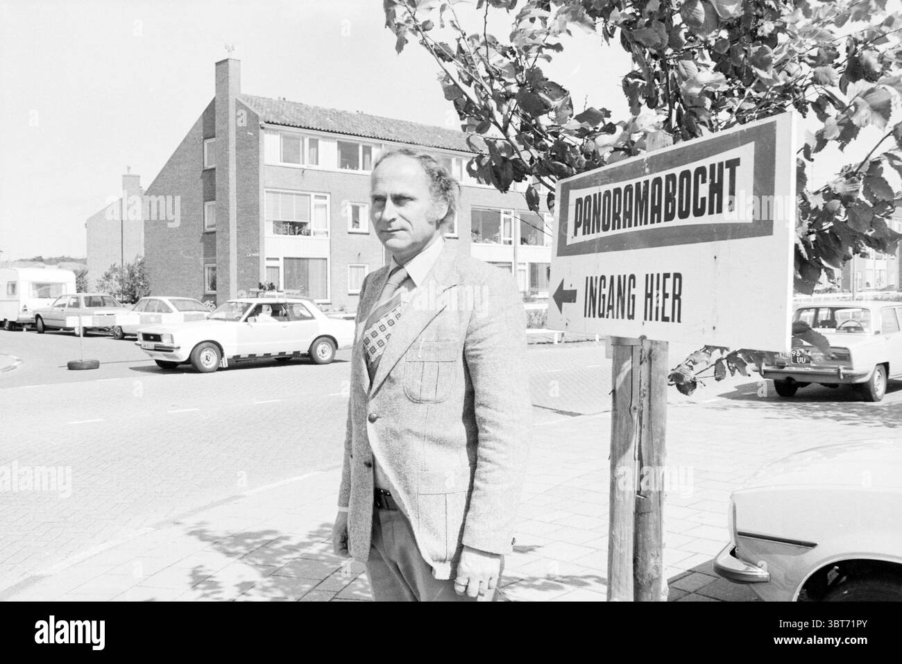 Homme au panneau indiquant l'entrée du virage panoramique du circuit de Zandvoort, Whizgle News, Dutch Desk, pays-Bas, 1950 - 2000 en 1978. Ces rubriques apparaissent dans l'image. Dans un cadre urbain animé, un homme se tient bien en vue au premier plan, dégageant un air de confiance. Il est bien habillé dans un costume de couleur claire, complété par une cravate à motifs qui ajoute une touche de personnalité à sa tenue. Son expression est focalisée, suggérant qu'il est profondément dans la pensée ou engagé dans un but particulier. La toile de fond présente une série de bâtiments résidentiels, caractérisés par un archit simple et moderne Banque D'Images
