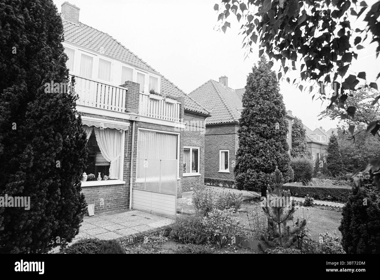 Extérieur Ramplaan 86-106 Haarlem Ramplaan pays-Bas, Whizgle News, Dutch Desk, pays-Bas, 1950 - 2000 on 28-09-1992. Voici les rubriques de l'image. La scène présente un quartier résidentiel tranquille caractérisé par une maison en briques soignée de deux étages qui dispose d'un toit à pignons distinctif. La façade est ornée de rideaux de couleur claire visibles à travers de grandes fenêtres rectangulaires, qui apportent une touche de chaleur à la structure. Au premier plan, la verdure méticuleusement entretenue comprend de hautes haies vert foncé qui encadrent les côtés de la maison. Ces haies contrastent avec les arbustes inférieurs, cre Banque D'Images