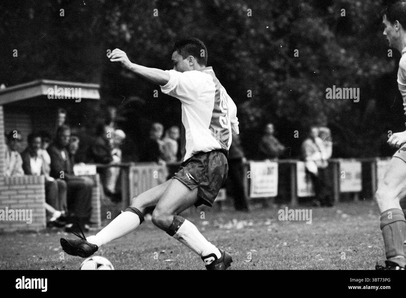 Football DIOS - Nieuw Vennep, Whizgle News, Dutch Desk, pays-Bas, 1950 - 2000 le 19-09-1992. Ce sont les éléments de l'image. Dans un cadre extérieur dynamique, deux athlètes dominent la scène, engagés dans un moment intense d'un match de football. Un joueur, positionné au premier plan, est capturé à mi-coup, étendant une jambe avec concentration tandis que l'autre reste fermement planté sur le sol. Il porte un maillot léger à manches courtes avec un design subtil, ainsi qu'un short contrasté qui ajoute à l'énergie du mouvement. Les cheveux du joueur sont courts, ajoutant à l'esthétique athlétique Banque D'Images