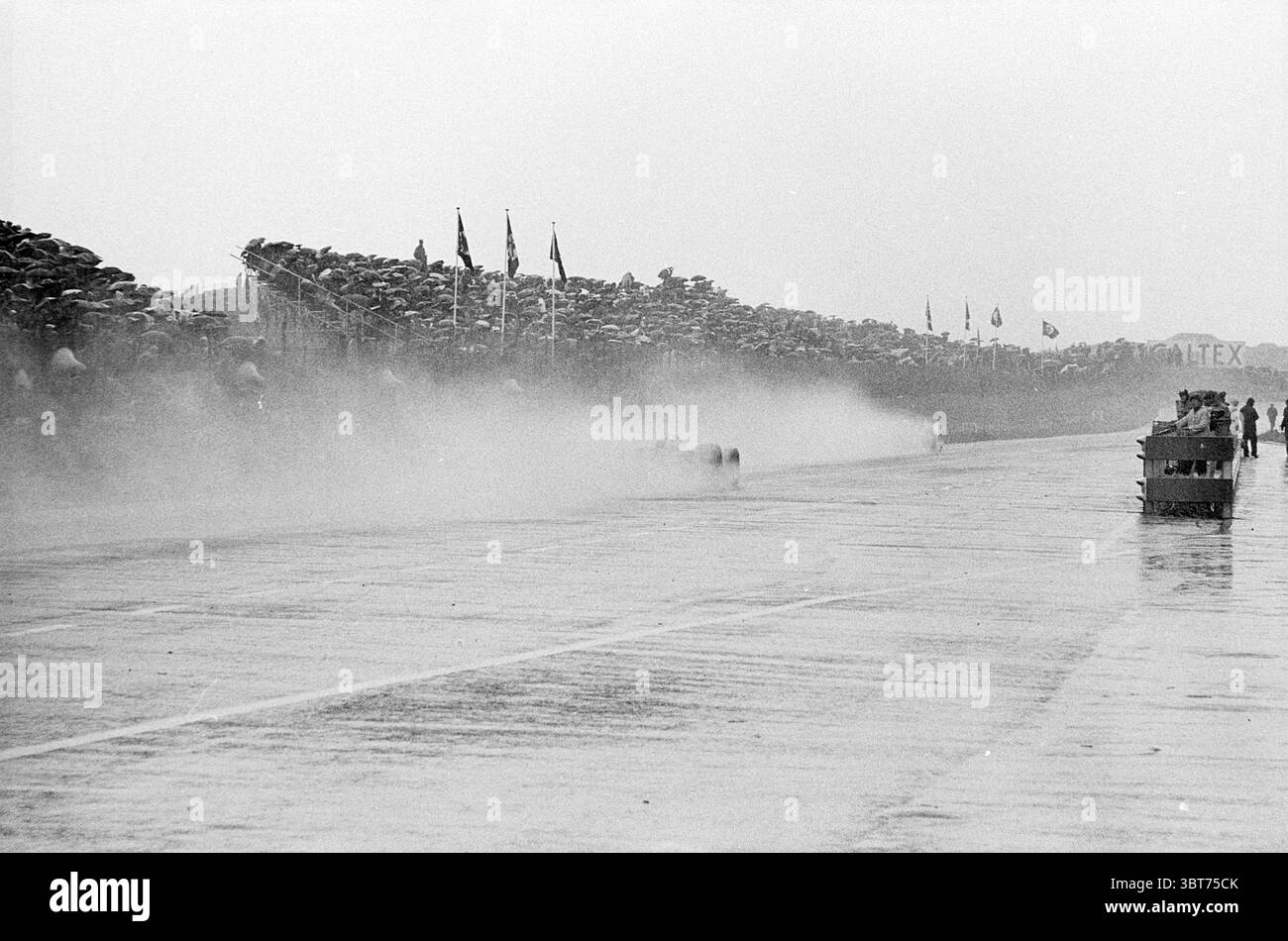 Course automobile sur le circuit de Zandvoort Zandvoort, Whizgle News, Dutch Desk, pays-Bas, 1950 - 2000 en 1968. L'image montre ces rubriques. La scène capture un moment dynamique et énergique lors d'un événement de course, sur fond de ciel gris et couvert. La surface humide de l'hippodrome brille sous la diffusion de la lumière, créant une qualité réfléchissante qui améliore l'atmosphère de vitesse et d'urgence. Au premier plan, un flou de véhicules de course se précipite, laissant derrière eux un panache de pulvérisation et de brume qui se mélange à la pluie sur l'asphalte. Les lignes épurées des voitures évoquent une sensation de mouvement Banque D'Images