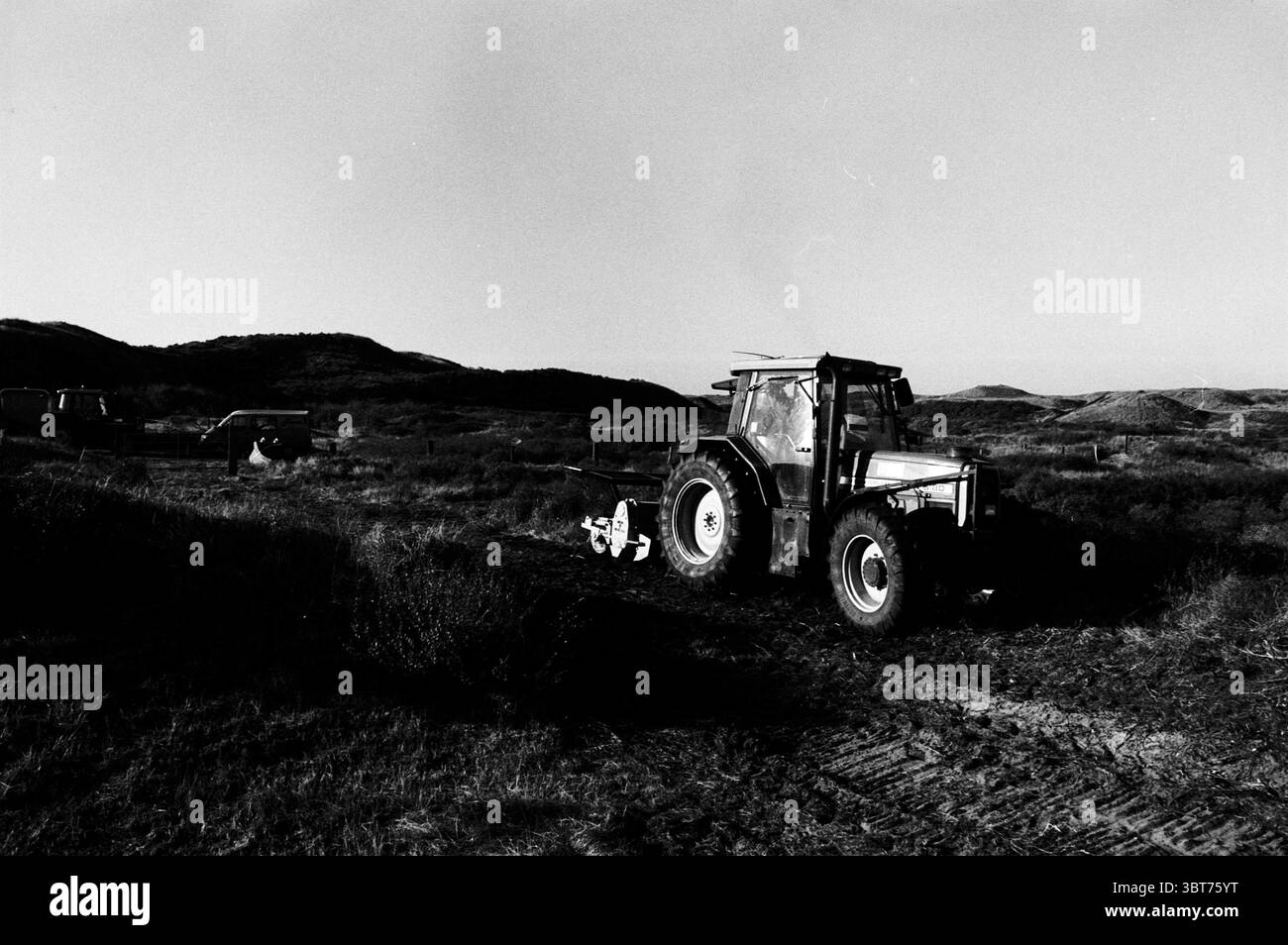 Dune excavation Duin & Kruidberg Santpoort Santpoort, Whizgle News, Dutch Desk, pays-Bas, 1950 - 2000 on 03-11-1997. L'image contient ces rubriques. La scène dépeint un paysage rural dominé par un tracteur robuste, qui occupe le premier plan. Ce véhicule est doté d'une carrosserie métallique robuste, présentant des éléments altérés qui impliquent une utilisation au fil du temps. Le tracteur est peint dans un ton discret, probablement une combinaison de gris poussiéreux et de vert délavé, avec ses roues de taille significative pour gérer le terrain accidenté. Autour du tracteur, le paysage est ouvert et vaste, suggérant un vaste champ Banque D'Images