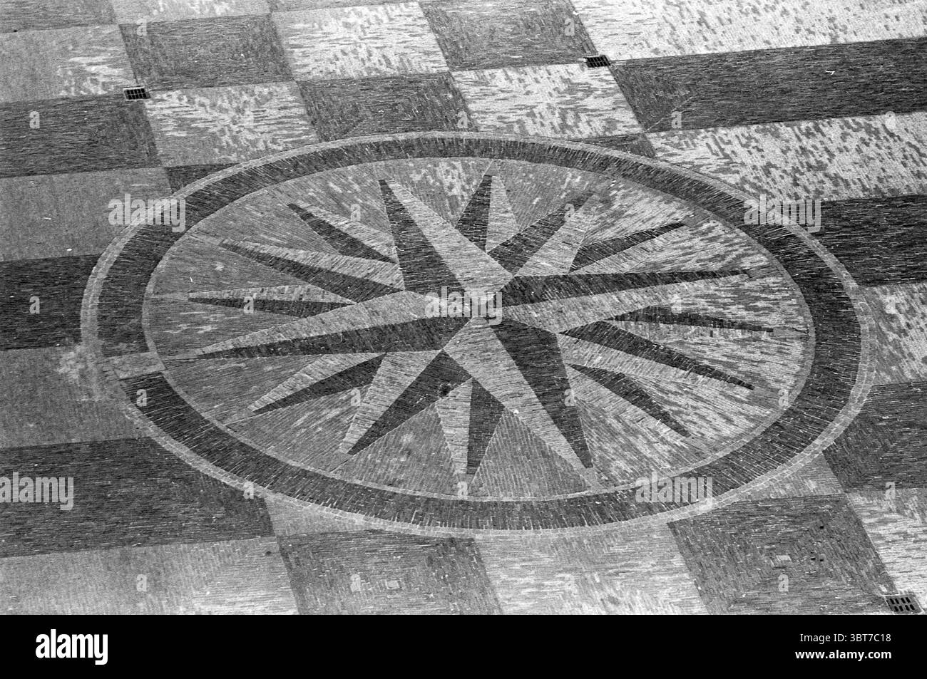 Précurseur Wind Rose sur la Grote Markt Haarlem Grote Markt pays-Bas, Whizgle News, Dutch Desk, pays-Bas, 1950 - 2000 en 1966. Ce sont les éléments de l'image. La scène présente un design de sol saisissant caractérisé par une rose de boussole circulaire en son centre, entourée de tuiles carrées alternées. La rose de la boussole présente une série de points triangulaires rayonnant à partir de son centre, créant un motif dynamique semblable à une étoile avec des angles vifs. La palette de couleurs est principalement monochrome, avec différentes nuances de gris et de noir, insufflant un sentiment d'intemporalité et d'élégance. Le surr Banque D'Images
