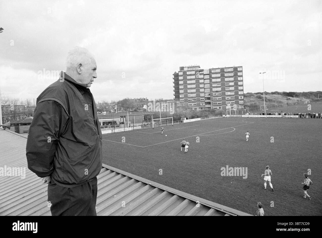 Conseiller Meijer en visite à Stormvogels IJmuiden pays-Bas, Whizgle News, Dutch Desk, pays-Bas, 1950 - 2000 on 09-11-1991. Ces rubriques apparaissent dans l'image. La scène montre un homme debout sur un toit, regardant vers le bas sur un terrain de football couvert d'herbe. Il porte une veste sombre, et son expression faciale semble contemplative, peut-être en réflexion sur l'action ci-dessous. Le terrain lui-même est animé, avec plusieurs joueurs en maillots aux couleurs vives engagés dans un match, leurs mouvements dynamiques et énergiques. Autour du champ sont des taches de vert sourd, faisant allusion aux pluies récentes, et au large de la Banque D'Images