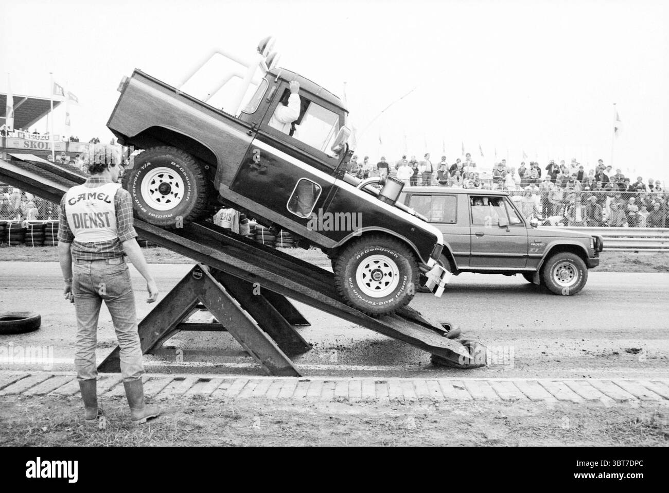 4 roues sur le circuit Zandvoort circuit Zandvoort Zandvoort, Whizgle News, Dutch Desk, pays-Bas, 1950 - 2000 on 08-09-1985. L'image inclut ces rubriques. La scène capture un moment dynamique lors d'un événement extérieur, probablement une compétition de sport automobile compte tenu du contexte. Au premier plan, un véhicule tout-terrain robuste est positionné à un angle sur une rampe de fortune, suggérant qu'il vient de franchir des obstacles ou démontre ses capacités. Le camion présente une palette de couleurs bicolores, avec une carrosserie noire frappante contrastée par une section plus légère, améliorant son apparence robuste. À gauche, a Banque D'Images
