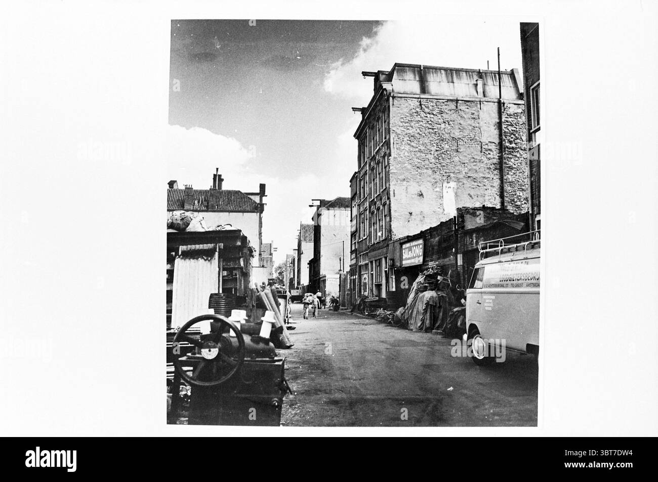 The Jewish Houttuinen Amsterdam Amsterdam pays-Bas., Whizgle News, Dutch Desk, pays-Bas, 1950 - 2000. Ces rubriques apparaissent dans l'image. La scène capture une ruelle urbaine étroite bordée de bâtiments en briques vieilles, dont beaucoup présentent des signes d'usure, tels que la peinture écaillée et les façades qui s'effondrent. La rue pavée est légèrement inégale, contribuant à un sentiment de charme historique. D'un côté, une collection de matériaux jetés et de structures de fortune laisse entrevoir un passé animé ; des tas de débris et d'ordures créent une atmosphère légèrement chaotique. Un vieux véhicule, probablement une camionnette, garé à th Banque D'Images