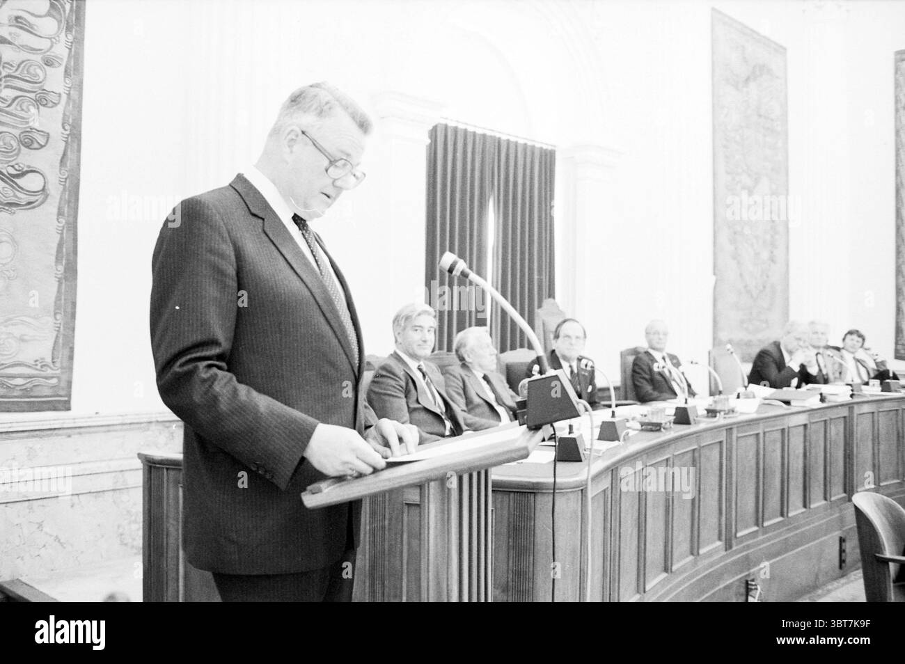 Adieu aux députés de la provincial House Prov. États Prov Water Management provincial House, Whizgle News, Dutch Desk, pays-Bas, 1950 - 2000 on 17-05-1982. L'image contient ces rubriques. Dans un cadre formel d'Assemblée, un homme se tient debout sur un podium en bois, engageant avec un public assis derrière lui. Il porte un costume sombre avec une chemise blanche et une cravate, dégageant un sentiment d'autorité et de confiance. L'homme semble concentré et sérieux, prononçant un discours alors qu'il regarde ses notes ou son discours sur le podium. Derrière lui, un groupe d'individus assis occupe une disposition semi-circulaire, Banque D'Images