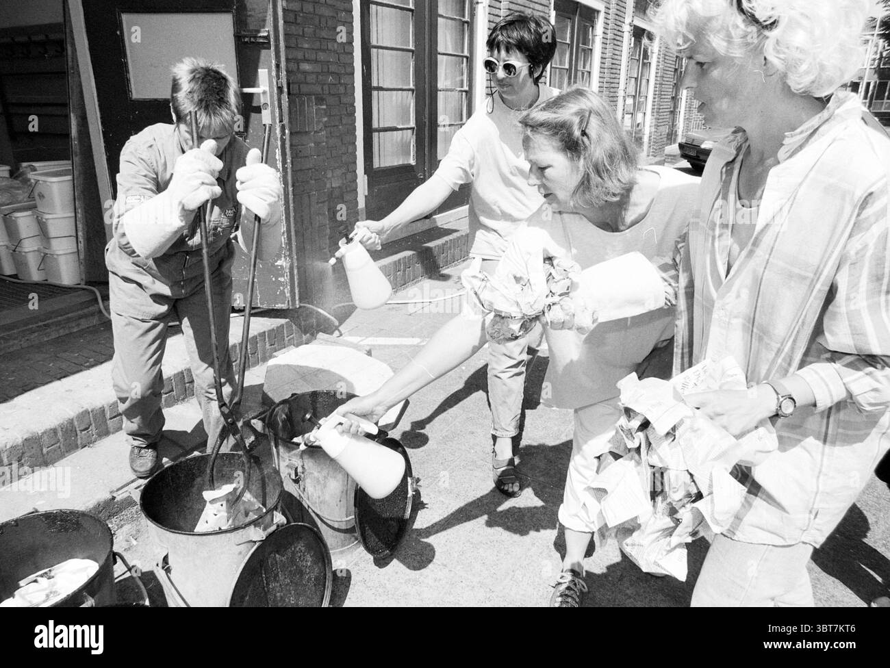 Cuisson céramique Raku IJmuiden IJmuiden pays-Bas, Whizgle News, Dutch Desk, pays-Bas, 1950 - 2000 le 30-05-1997. L'image inclut ces rubriques. La scène représente un cadre extérieur animé, probablement dans une zone urbaine, caractérisé par un sol pavé texturé. Un groupe de quatre personnes s'engage dans une tâche de nettoyage ou de jardinage, faisant preuve d'un sens du travail d'équipe et de l'engagement communautaire. Au premier plan, une personne portant un uniforme de travail, y compris une chemise et un pantalon de couleur claire, se concentre sur l'utilisation d'un outil pour remuer ou gérer un contenant, éventuellement rempli de déchets ou de débris. Thi Banque D'Images