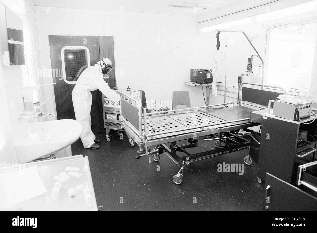 Quarantaine Croix-Rouge B'wijk Croix-Rouge Croix-Rouge Hôpital Beverwijk pays-Bas, Whizgle News, Dutch Desk, pays-Bas, 1950 - 2000 on 04-08-1989. L'image inclut ces rubriques. La scène représente un environnement clinique stérile, probablement dans un établissement médical. La palette de couleurs globale est dominée par des nuances de blanc, de gris et de noir, évoquant un sentiment de propreté et de précision. Au centre, il y a un lit d'hôpital sur roulettes, avec un cadre métallique et un matelas avec une surface simple et plate. La position du lit est légèrement inclinée, indiquant qu'il est prêt pour une utilisation immédiate. Banque D'Images