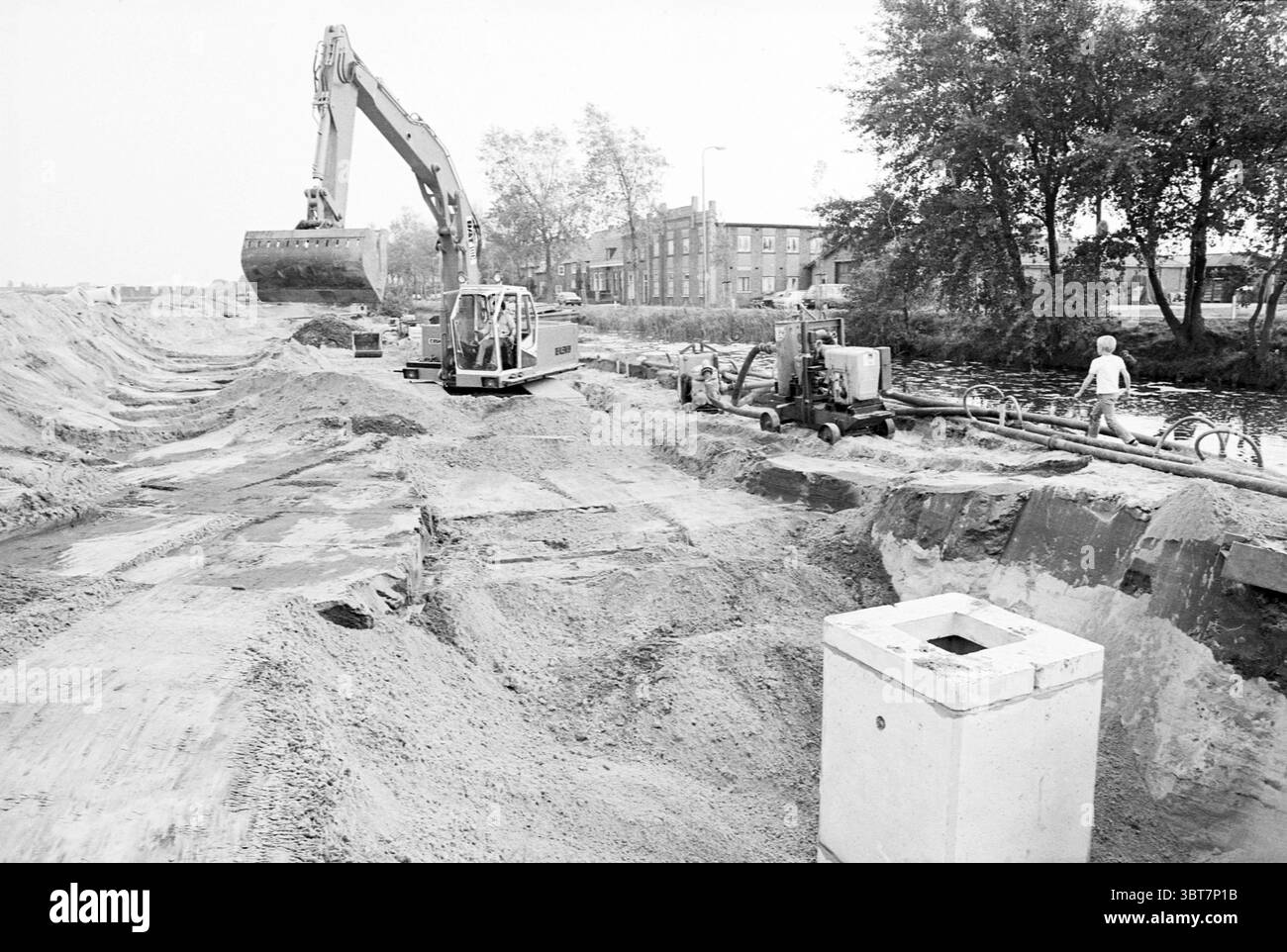 Usine d'assainissement Wilhelminalaan usine Hillegom usine Hillegom Wilhelminalaan, Whizgle News, Dutch Desk, pays-Bas, 1950 - 2000 le 25-09-1980. L'image montre ces rubriques. La scène capture un chantier de construction, dominé par une palette monochromatique, mettant l'accent sur les nuances de gris et les tons sourds. Une grande pelle hydraulique se trouve au premier plan, son bras robuste étendu vers un monticule de terre, tandis que son godet est prêt à ramasser plus de terre. À proximité, un véhicule plus petit semble être en service, travaillant aux côtés de machines qui suggèrent un réseau de tuyaux. Le sol est inégal et couvert de tas de san Banque D'Images