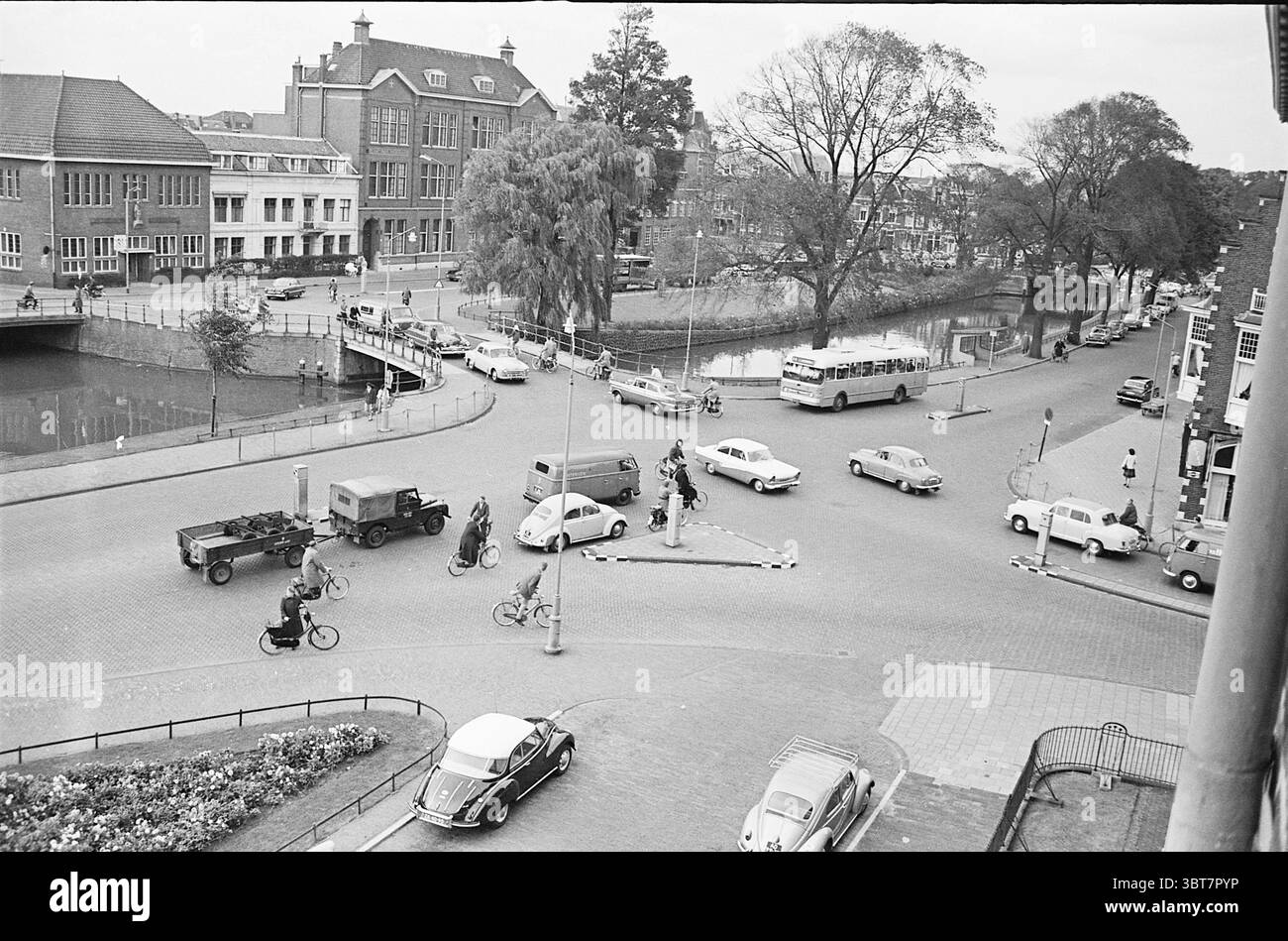 Crossroads Raaks Traffic Safe Traffic Haarlem Raaks pays-Bas, Whizgle News, Dutch Desk, pays-Bas, 1950 - 2000 on 12-09-1961. L'image contient ces rubriques. La scène capture une intersection urbaine animée depuis une perspective élevée. Un îlot de circulation circulaire est visible au centre, avec quelques piétons naviguant autour d'elle. Divers véhicules traversent l'intersection, y compris des voitures du milieu du XXe siècle, certaines compactes et arrondies, suggérant une sensation nostalgique. Un camion classique, légèrement plus grand, est garé sur le côté, évoquant la vie quotidienne de l'époque. S Banque D'Images