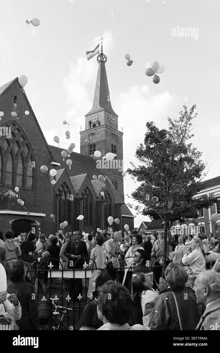 Réouverture de Maartenskerk Hillegom (lâcher des ballons devant l'église), Whizgle News, Dutch Desk, pays-Bas, 1950 - 2000. Ce sont les éléments de l'image. La scène capture un rassemblement communautaire dynamique à l'extérieur d'une église en briques frappante caractérisée par son grand clocher et son horloge. L'architecture, avec ses fenêtres ornées et ses arcs pointus, ajoute un sentiment de grandeur au cadre. Au premier plan, une foule nombreuse se rassemble, hommes et femmes de différents âges, tous engagés et animés. Ils sont habillés dans un mélange de vêtements décontractés et semi-formels, suggérant un événement important. Le Banque D'Images