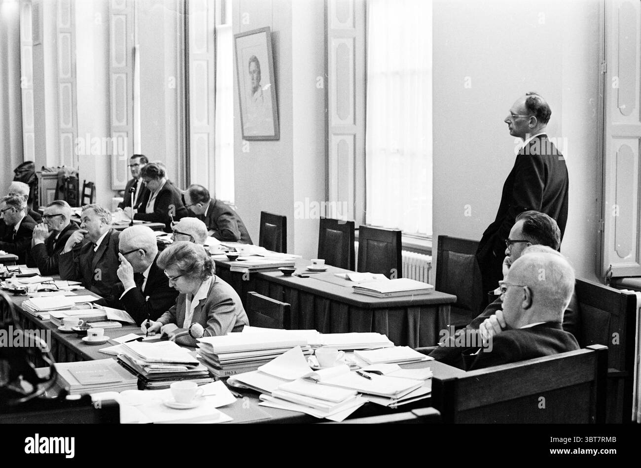 Budget Deb. Haarlem 1962 conseils municipaux, Whizgle News, Dutch Desk, pays-Bas, 1950 - 2000 on 19-11-1962. Ces rubriques apparaissent dans l'image. La scène représente un rassemblement formel dans une grande salle élégamment conçue. Le cadre transmet un sentiment d'autorité et de professionnalisme, caractérisé par de hauts plafonds et de hautes fenêtres qui permettent à la lumière naturelle de circuler, projetant une douce lueur dans l'espace. Une longue table en bois est positionnée au centre, bordée d'individus engagés dans une discussion sérieuse. Les personnes assises autour de la table, un mélange d'hommes et de femmes, présentent une gamme d'expressions Banque D'Images
