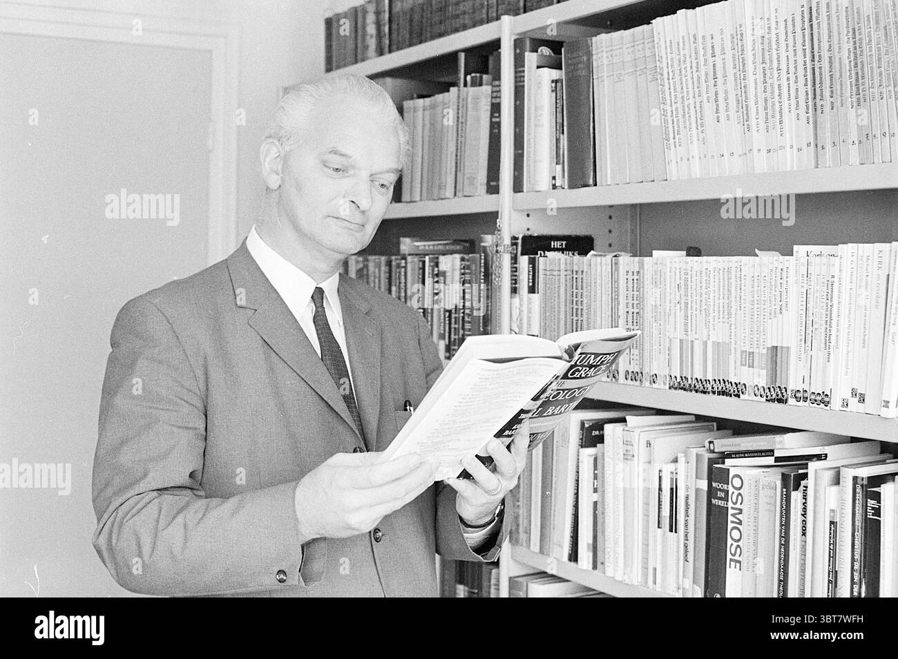 Pastor van Dijk clergé, Whizgle News, Dutch Desk, pays-Bas, 1950 - 2000 le 06-09-1971. L'image inclut ces rubriques. Un homme se tient dans un cadre semblable à une bibliothèque, entouré d'étagères soigneusement organisées remplies d'une variété de livres. Sa tenue est formelle, avec un costume sur mesure qui suggère un environnement professionnel ou académique. La palette de couleurs est principalement monochromatique, avec des nuances de gris qui dominent la scène, soulignant une ambiance classique et sérieuse. L'éclairage est doux et uniforme, projetant de douces ombres qui mettent en valeur les contours de son visage et la texture des livres. Le m Banque D'Images