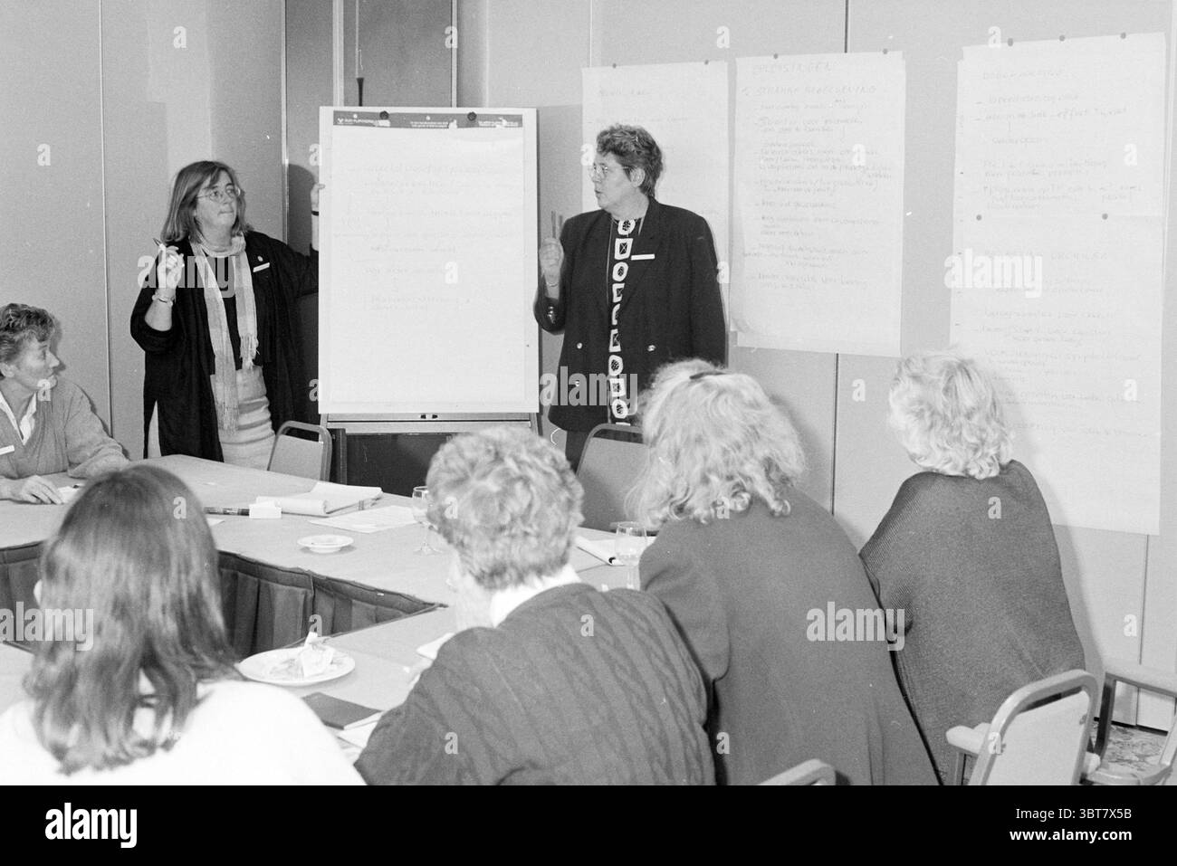 Réunion des femmes agricoles, Whizgle News, Dutch Desk, pays-Bas, 1950 - 2000 le 03-10-1994. Ces rubriques apparaissent dans l'image. Un groupe de personnes est assis autour d'une table rectangulaire, engagé dans ce qui semble être une discussion ou une réunion. La table est encombrée de blocs-notes, de stylos et de petites assiettes qui font allusion à des rafraîchissements, tels que des collations ou des pâtisseries. Vers l'avant, deux personnes se tiennent debout et font une présentation active au groupe. L'un porte un blazer foncé et a une posture expressive, en utilisant ses mains pour l'accent. L'autre est habillé dans une tenue plus décontractée, combinant les deux prof Banque D'Images