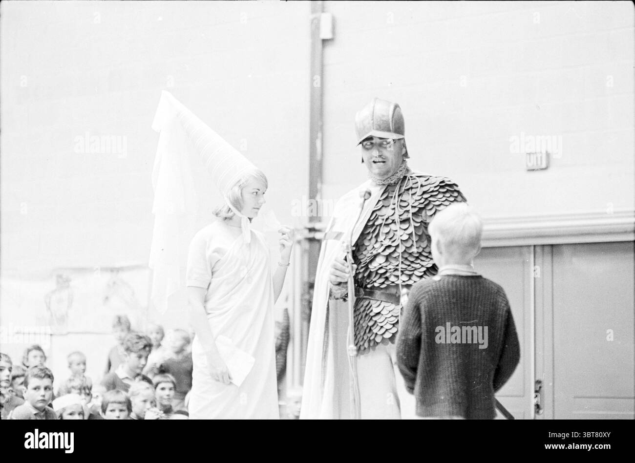 Instuif-stuif Jeux d'enfants Jeux de vacances jours de vacances camp de vacances, Whizgle News, Dutch Desk, pays-Bas, 1950 - 2000 le 22-08-1963. Ces rubriques sont illustrées dans l'image. La scène capture un instant d'une performance, situé dans un grand espace intérieur qui se sent vivant et engagé. Au premier plan, deux figures sont bien en évidence. Sur la gauche se trouve une femme vêtue de blanc, sa tenue rappelant la mode grecque antique, avec des draperies fluides qui suggèrent la grâce et l'élégance. Elle porte un casque distinctif qui se rétrécit jusqu'à un point, ajoutant un élément de fantaisie à son apparence. Sur le Banque D'Images