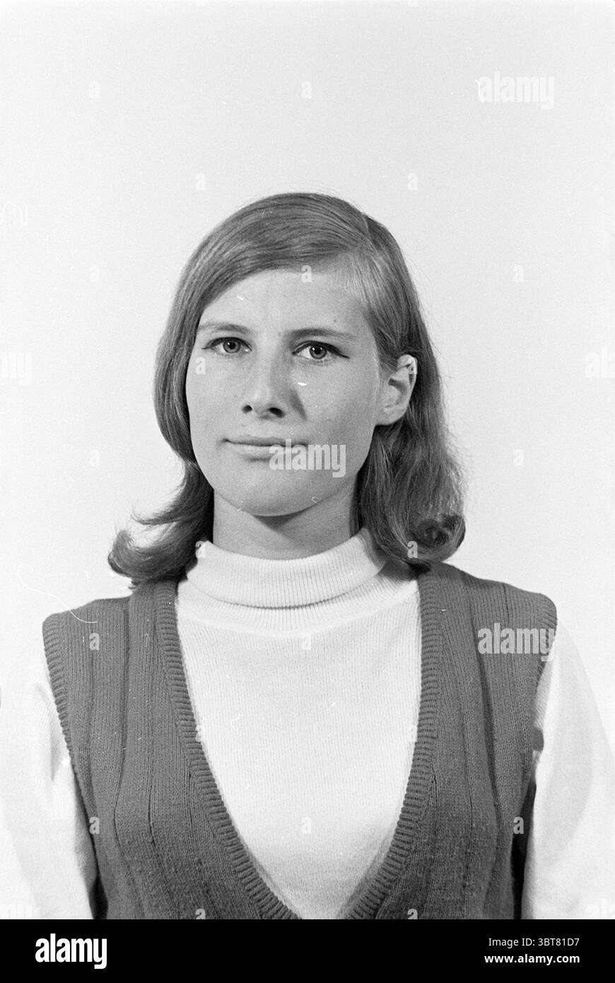 Portrait d'une femme., Whizgle News, Dutch Desk, pays-Bas, 1950 - 2000. L'image inclut ces rubriques. La scène met en scène une jeune femme avec une expression réfléchie. Ses cheveux sont marron châtaignier, coiffés de vagues douces qui encadrent son visage. Elle porte un gilet tricoté sans manches sur un col roulé, ce qui contribue à une atmosphère rétro avec sa combinaison de textures et de couches. Le gilet affiche un motif subtil et nervuré, ajoutant de la profondeur à l'ensemble. L'arrière-plan est minimaliste et léger, créant un contraste qui souligne sa présence. L'éclairage est doux et uniforme, jetant Sha doux Banque D'Images