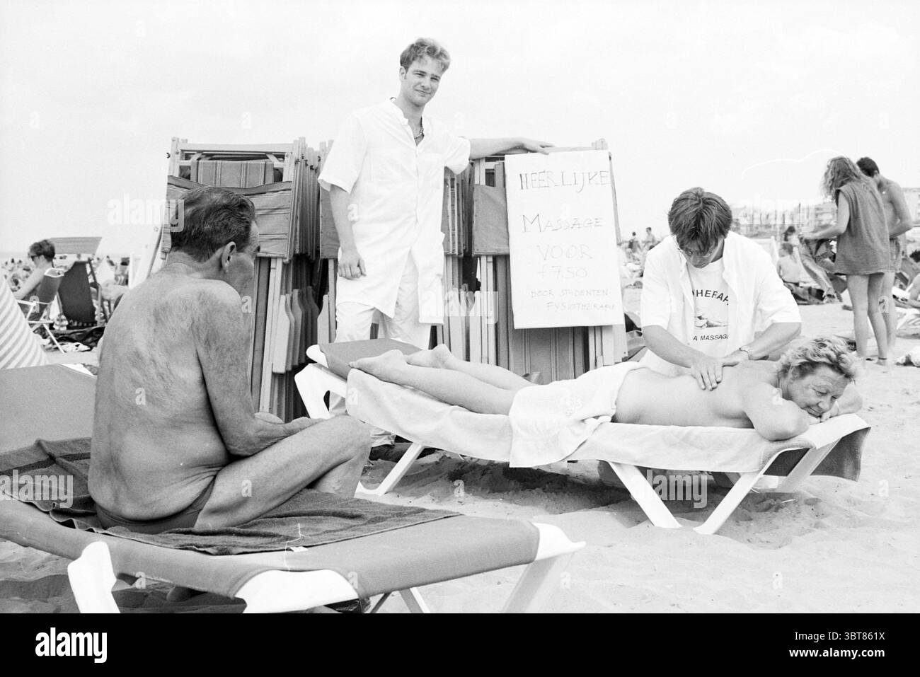 Massage sur la plage Zandvoort Zandvoort, Whizgle News, Dutch Desk, pays-Bas, 1950 - 2000 le 19-07-1994. Ces rubriques sont illustrées dans l'image. La scène capture un cadre de plage animé, rempli de chercheurs de soleil profitant du temps chaud. Au premier plan, un homme au corps bronzé et embrassé par le soleil s'incline sur une chaise longue blanche, le dos face au spectateur. Le contraste saisissant entre sa peau et le blanc de la chaise crée un impact visuel saisissant. À proximité, une autre personne est allongée à plat sur une chaise longue similaire, semblant profiter d'un massage. Cette personne a les cheveux plus longs, partiellement obscu Banque D'Images