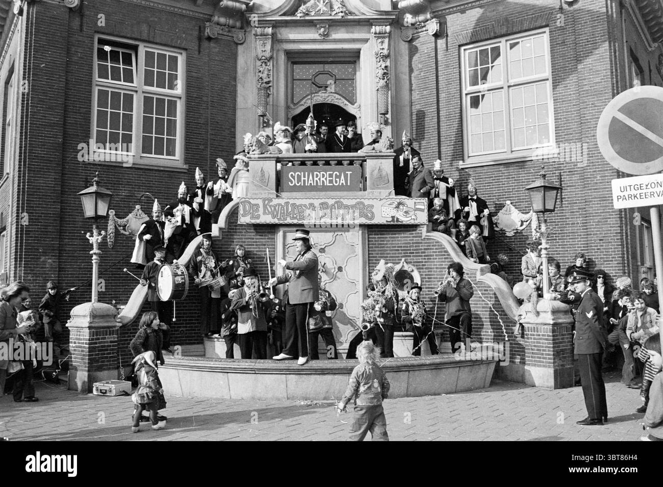 Carnival Parade Zandvoort Carnival, Whizgle News, Dutch Desk, pays-Bas, 1950 - 2000 le 28-02-1976. L'image montre ces rubriques. La scène est un rassemblement animé en plein air, centré autour d'un escalier orné menant à un grand bâtiment, présentant une façade complexe. L'architecture comporte des éléments décoratifs, peut-être des sculptures en pierre, et de multiples grandes fenêtres qui reflètent l'activité au sein de la structure. Dans les escaliers, un groupe diversifié d'individus occupe divers endroits. Certains se tiennent fièrement debout, tandis que d'autres sont assis ou appuyés contre les balustrades. La tenue vestimentaire varie, indiquant un festi Banque D'Images