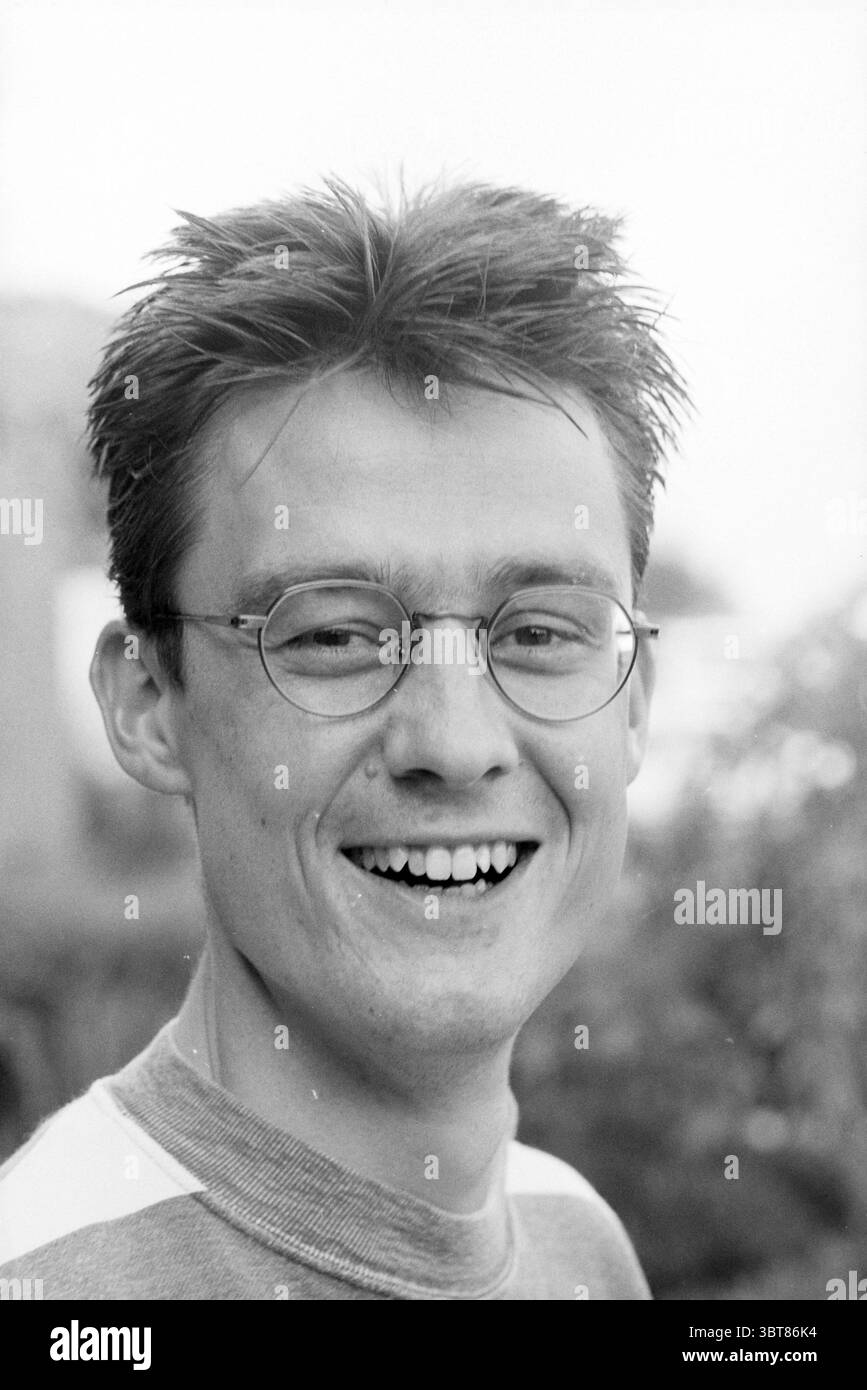 Tim Huizinga Bennebroek, Whizgle News, Dutch Desk, pays-Bas, 1950 - 2000 le 21-08-1994. Ces rubriques apparaissent dans l'image. Dans la scène, un jeune homme sourit, saisissant un moment de joie et de chaleur. Il a des cheveux courts et pointus qui se démarquent, suggérant une personnalité vivante et énergique. Ses lunettes rondes reposent confortablement sur son visage et mettent en valeur ses yeux expressifs. L'arrière-plan est légèrement flou, évoquant une verdure naturelle, ce qui ajoute une atmosphère sereine à la composition globale. L'homme est habillé d'un pull de couleur claire avec un motif subtil, créant un amical et approachab Banque D'Images