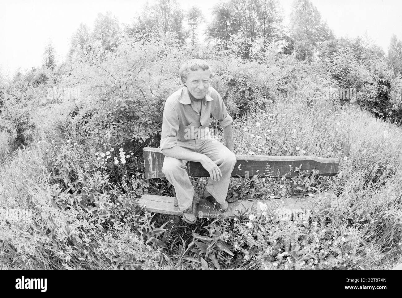 Biologiste dans le jardin environnemental jardins et parcs Hoofddorp, Whizgle News, Dutch Desk, pays-Bas, 1950 - 2000 sur 07-06-1978. Ce sont les éléments de l'image. Dans un cadre naturel serein, un homme est assis sur un banc rustique en bois, entouré d'une étendue luxuriante de fleurs sauvages et de hautes herbes. Le banc, épuré et simple, est positionné au milieu d'une parcelle de flore florissante, qui ajoute de la vitalité à la scène avec des nuances variées de jaune, blanc et violet. L’homme apparaît contemplatif, portant une chemise et un pantalon de couleur claire qui se fondent harmonieusement avec l’environnement. Ses cheveux, t Banque D'Images