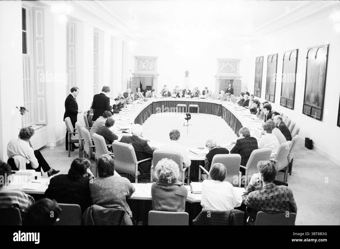 Budget Conseil municipal de Haarlem Conseil municipal de Haarlem, Whizgle News, Dutch Desk, pays-Bas, 1950 - 2000 le 23-11-1987. L'image contient ces rubriques. La scène représente une grande réunion dans une salle spacieuse et bien éclairée caractérisée par une disposition circulaire des tables. Les murs de la salle sont ornés de plusieurs grandes œuvres d'art encadrées ou de portraits, ajoutant une atmosphère formelle. Un groupe diversifié d'individus s'assoit autour de la table, tous semblant engagés dans la discussion. Les participants, la plupart du temps vêtus d'une tenue professionnelle, sont positionnés de telle sorte qu'ils se font face, améliorant ainsi le sens de Banque D'Images