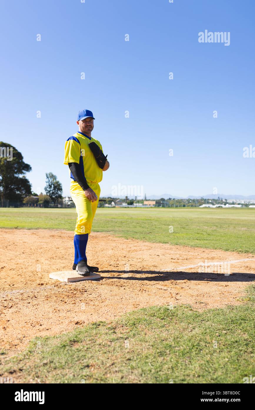 Joueur de baseball masculin en uniforme debout sur la première base au parc tenant un gant de baseball, espace copie Banque D'Images