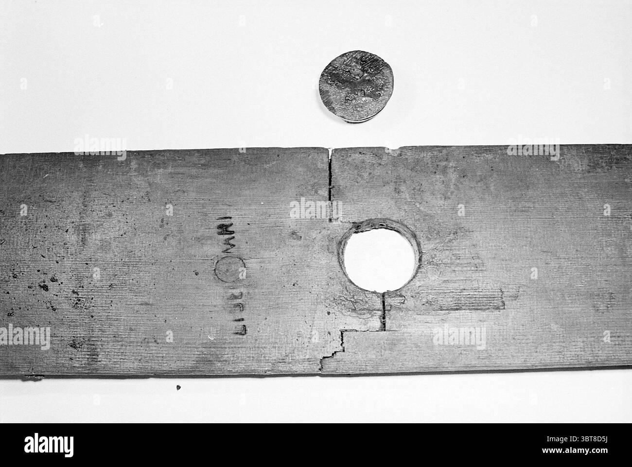 MRS Gordijn avec vieux tonneau de vin IJmuiden Archéologie, Whizgle News, Dutch Desk, pays-Bas, 1950 - 2000 le 08-01-1977. Ces rubriques sont illustrées dans l'image. La scène présente une vue rapprochée d'une planche de bois posée à plat, montrant une surface bien usée qui révèle la texture du bois. La planche est rectangulaire, avec des bords dentelés et des imperfections notables, telles que de petites fissures et un trou circulaire près d'une extrémité. Ce trou suggère l'utilisation, éventuellement pour une cheville ou une certaine forme de connexion. Juste au-dessus de la planche, il y a un objet rond et métallique qui semble être une pièce de monnaie. Il a un surf altéré Banque D'Images