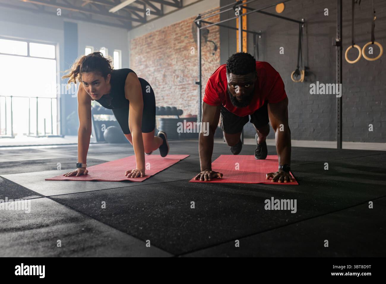 Couple diversifié effectuant une planche bras-jambe alternée sur des tapis rouges dans un studio de fitness avec une plate-forme de traction Banque D'Images