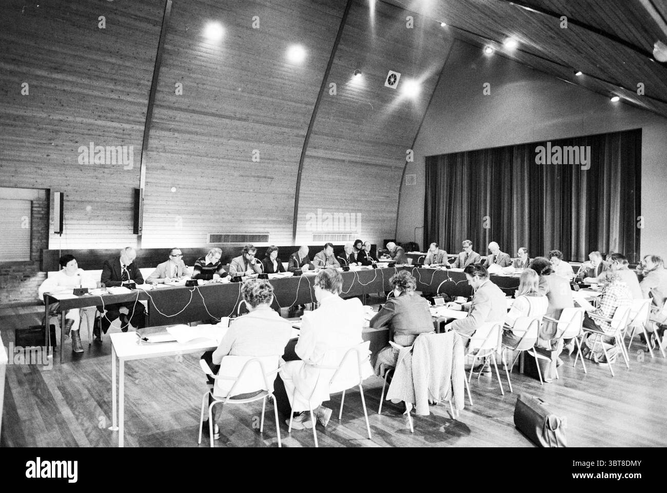 Aperçu de la réunion budgétaire (à Vrijburcht) Heemskerk réunions du conseil municipal de Heemskerk, Whizgle News, Dutch Desk, pays-Bas, 1950 - 2000 on 07-11-1977. Ces rubriques apparaissent dans l'image. Une salle de conférence spacieuse et moderne est remplie d'un groupe de personnes engagées dans une discussion. La salle dispose de hauts plafonds en bois qui ajoutent une atmosphère chaleureuse et accueillante, avec de grandes fenêtres laissant passer la lumière naturelle. Assis à une longue table se trouvent de nombreuses personnes, hommes et femmes, vêtues d'une tenue formelle. Certains se penchent en avant, participent activement, tandis que d'autres sont taki Banque D'Images
