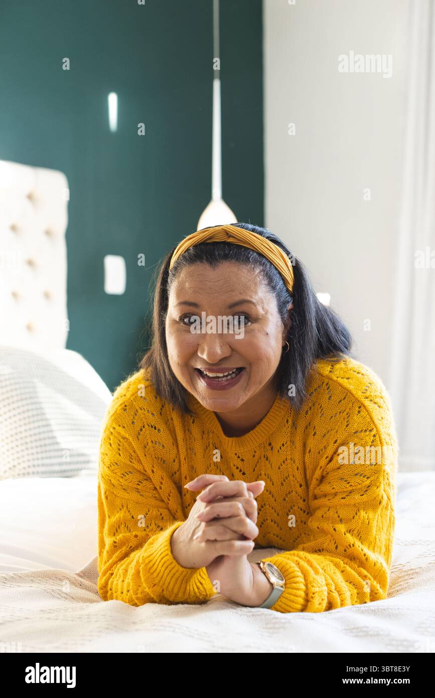 Femme couchée sur le ventre sur le lit dans la chambre avec des oreillers texturés portant un pull jaune et un bandeau Banque D'Images