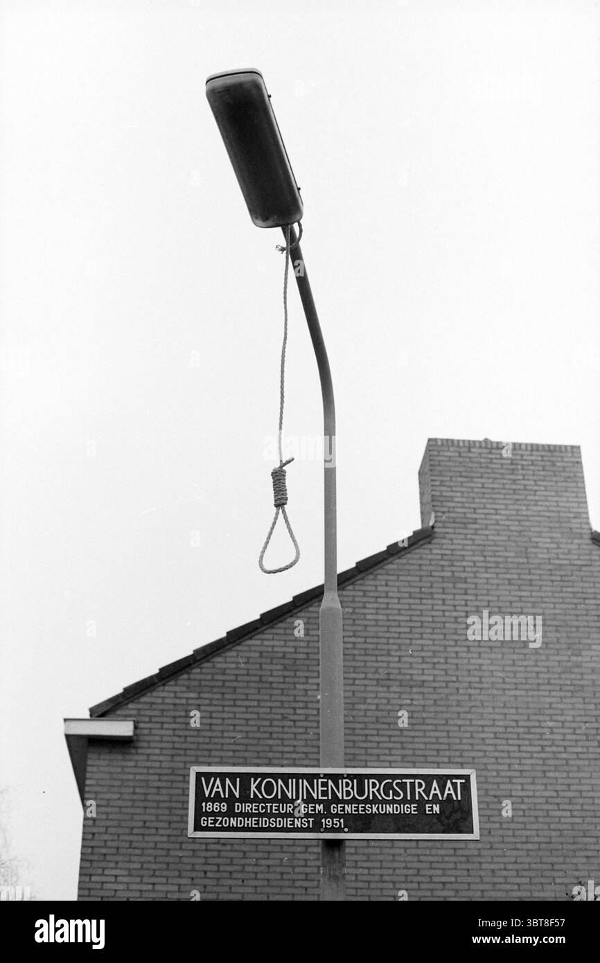 Lanterne avec nœud coulant sur la Van Konijnenburgstraat Haarlem. Lanternes Haarlem Van Konijnenburgstraat pays-Bas, Whizgle News, Dutch Desk, pays-Bas, 1950 - 2000 le 19-01-1987. Ce sont les éléments de l'image. La scène présente un environnement urbain sombre, dominé par les tons discrets d'un ciel gris qui projette une lumière sombre sur la zone. Un lampadaire solitaire se tient bien en évidence au premier plan, sa structure métallique polie mais montrant des signes d'âge. La lampe est éteinte, créant une sensation de calme. Accroché au lampadaire est un nœud coulant, ajoutant un élément obsédant au Banque D'Images