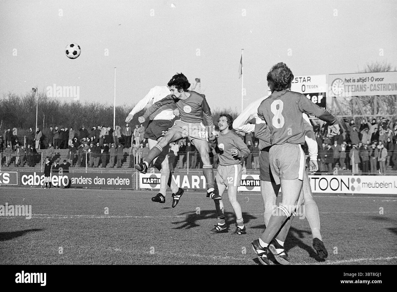 Telstar football match Velsen, Whizgle News, Dutch Desk, pays-Bas, 1950 - 2000 en 1972. L'image contient ces rubriques. Dans une scène dynamique de sports de plein air, un groupe d'athlètes est engagé dans un moment animé d'un match de football sur un terrain herbeux. Les joueurs, vêtus d'uniformes contrastés ; une équipe en maillots sombres et l'autre en teintes plus claires, sont activement impliqués dans le jeu. La figure centrale est aéroportée, capturée à mi-saut avec les bras tendus, visant à se connecter avec un ballon de football à carreaux noir et blanc. Son expression véhicule détermination et concentration. Autour de lui, coéquipier Banque D'Images