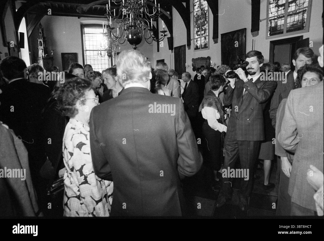 Rubans rain Haarlem Royal Honors Haarlem pays-Bas, Whizgle News, Dutch Desk, pays-Bas, 1950 - 2000 le 27-04-1990. Ces rubriques sont illustrées dans l'image. La scène présente un grand rassemblement de personnes dans un cadre intérieur élégant, caractérisé par de hauts plafonds ornés de poutres en bois. L’ambiance est animée, remplie de conversations et d’interactions animées. Des personnes de différents âges sont présentes, vêtues d'une tenue formelle. Beaucoup de femmes portent des robes qui vont de motifs floraux à des couleurs plus classiques et Unies, contribuant à une atmosphère vibrante, tandis que les hommes sont vus en costume Banque D'Images
