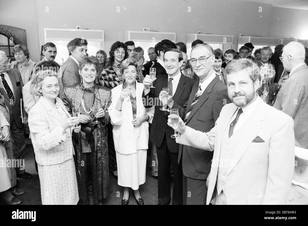 Ouverture Austral GEMS Kruisstraat ouverture ouverture commande Haarlem Kruisstraat pays-Bas, Whizgle News, Dutch Desk, pays-Bas, 1950 - 2000 on 02-11-1986. L'image inclut ces rubriques. Dans un rassemblement animé, un groupe diversifié de personnes se tient étroitement ensemble, formant un demi-cercle qui rayonne de chaleur et de camaraderie. Les individus affichent une gamme d'expressions, des sourires joviaux aux rires enthousiastes, créant une atmosphère accueillante. La palette de couleurs présente des tons classiques, avec beaucoup portant des costumes sombres ou des robes élégantes accentuées par des accessoires plus lumineux, comme des cravates ou Banque D'Images