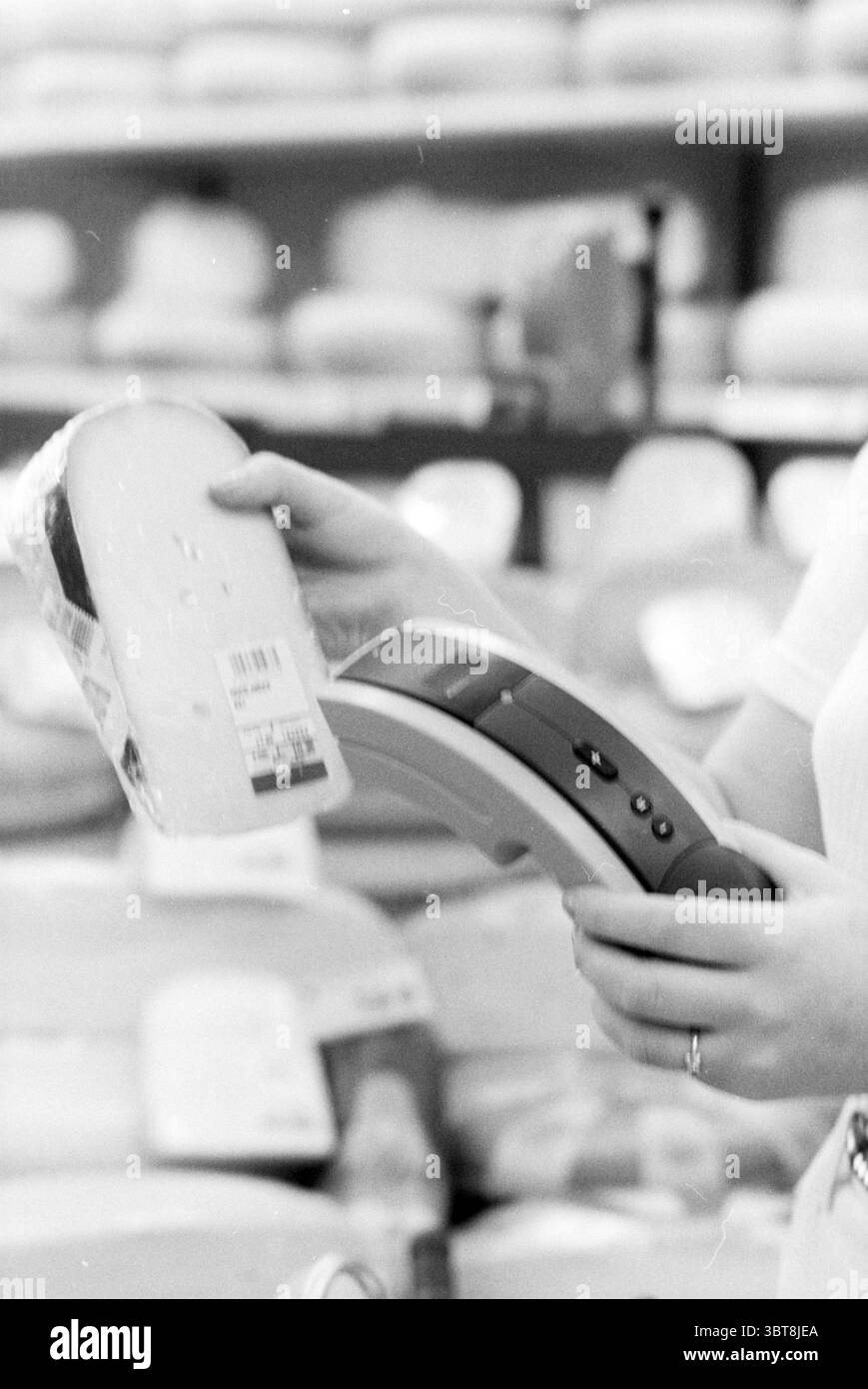 Lecteur de codes-barres AH Heemstede Heemstede pays-Bas, Whizgle News, Dutch Desk, pays-Bas, 1950 - 2000 sur 16-06-1994. Ces rubriques apparaissent dans l'image. Dans un environnement de vente au détail, une personne est engagée dans le processus de balayage d'un article. L'individu tient un lecteur portable, son design élégant avec une combinaison de formes incurvées et de boutons, suggérant la fonctionnalité et la facilité d'utilisation. L'autre main saisit un morceau de fromage emballé, partiellement visible, avec une surface lisse et brillante qui réfléchit la lumière douce. Les couleurs de l'emballage de fromage comprennent des jaunes crémeux et des verts subtils, indiquant Banque D'Images