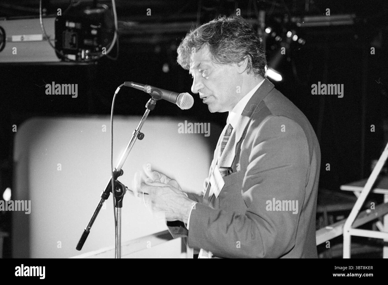 Conférence Mr. Hoet patronage, Whizgle News, Dutch Desk, pays-Bas, 1950 - 2000 le 24-06-1997. Ces rubriques apparaissent dans l'image. La scène capture une personne engagée dans la parole, debout devant un microphone tout en semblant communiquer passionnément. Il est habillé d'un costume bien ajusté, suggérant une atmosphère de formalité et de professionnalisme. Ses cheveux sont légèrement émoussés, indiquant peut-être un sentiment d'intensité ou de concentration dans le moment. L'arrière-plan est faiblement éclairé, avec une lueur douce des plafonniers éclairant le visage de l'enceinte tout en projetant de légères ombres. Ces lumières créent un contras Banque D'Images