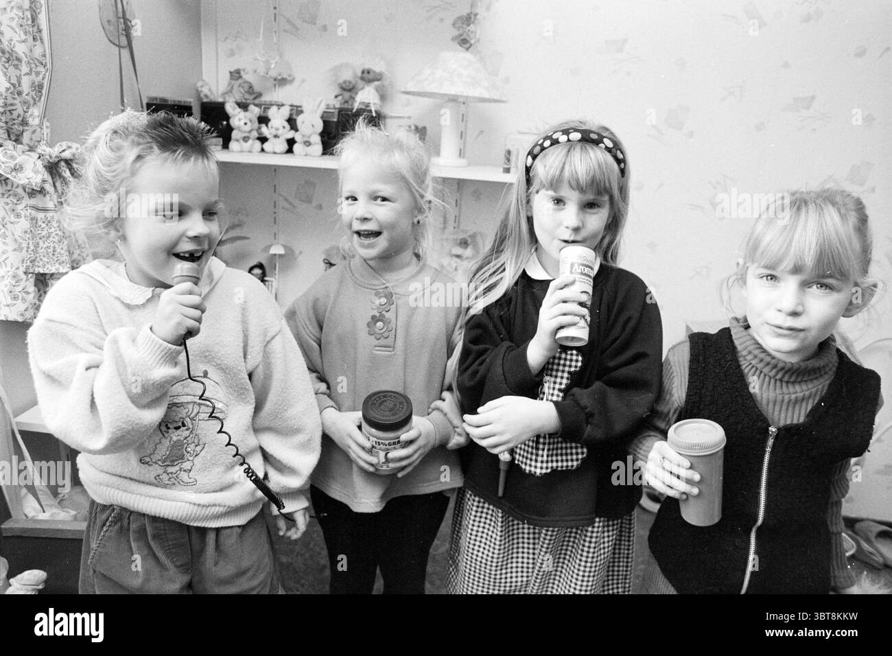 Quatre filles 'Bangles' Velserbroek, Whizgle News, Dutch Desk, pays-Bas, 1950 - 2000 le 09-12-1992. Voici les rubriques de l'image. Dans un cadre intérieur cosy, quatre enfants sont rassemblés, chacun dégageant une ambiance animée et ludique. Ils se tiennent proches les uns des autres, leurs expressions pleines de joie et d’excitation. Le premier enfant sur la gauche tient un petit micro à main, sa bouche ouverte en milieu de phrase, peut-être chantant ou parlant. Elle arbore un pull de couleur claire avec un dessin de personnage de dessin animé, contrastant avec les autres. Ses cheveux sont coiffés avec une légère vague, ajoutant une touche ludique. Banque D'Images