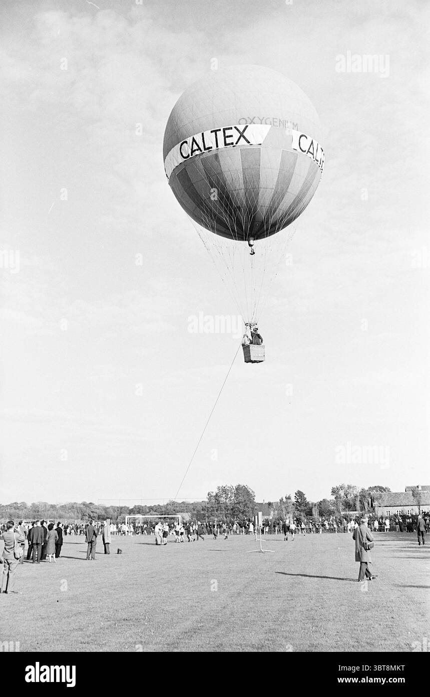 Balloon Ascent Heemskerk Heemskerk, Whizgle News, Dutch Desk, pays-Bas, 1950 - 2000 le 01-09-1963. L'image montre ces rubriques. La scène capture un événement extérieur animé centré autour d'une montgolfière. Le ballon, bien en évidence, présente un jeu de couleurs orange et rouge vives avec une forme arrondie, sa canopée s'étendant haut contre un ciel bleu clair parsemé de nuages doux et blancs. Ci-dessous, un panier est suspendu au ballon, suspendu par des cordes robustes. Le cadre semble être un champ herbeux, animé par l'activité. Une foule de gens, habillés dans un mélange de décontracté et légèrement formel Banque D'Images