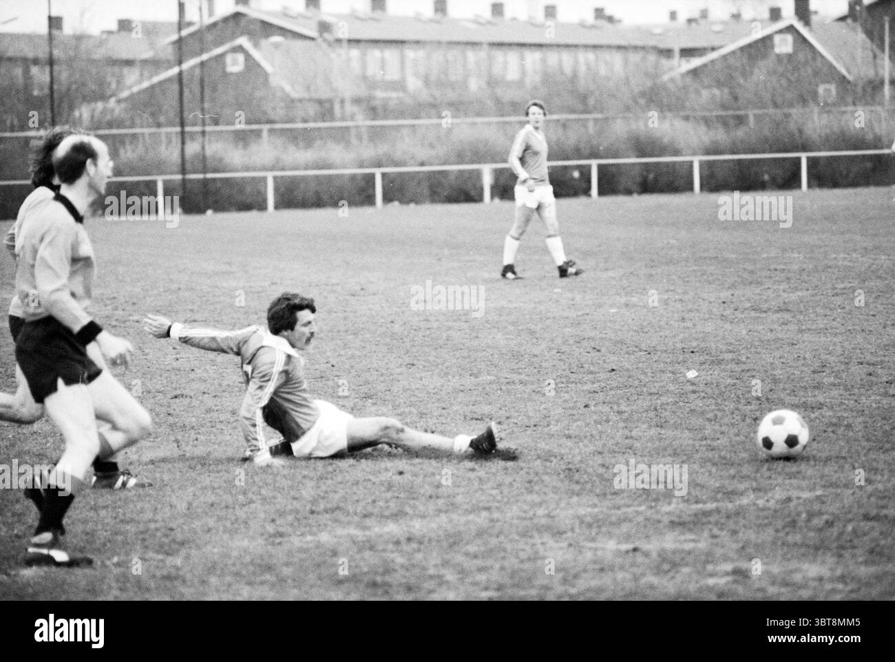 Stormvogels - Sizo Football V.S.V. Velsen Stormvogels, Whizgle News, Dutch Desk, pays-Bas, 1950 - 2000 on 07-05-1979. Ces rubriques sont illustrées dans l'image. La scène capture un moment dynamique sur un terrain herbeux, où un groupe de joueurs est engagé dans un match de football. Le ciel est couvert, projetant une lumière silencieuse sur la zone, ce qui renforce l'atmosphère sombre et graveleuse du jeu. Deux joueurs sont en évidence au premier plan. L'un, portant un maillot orange, glisse sur le sol pour tenter d'atteindre le ballon, qui est juste hors de sa portée. Sa posture transmet un s. Banque D'Images
