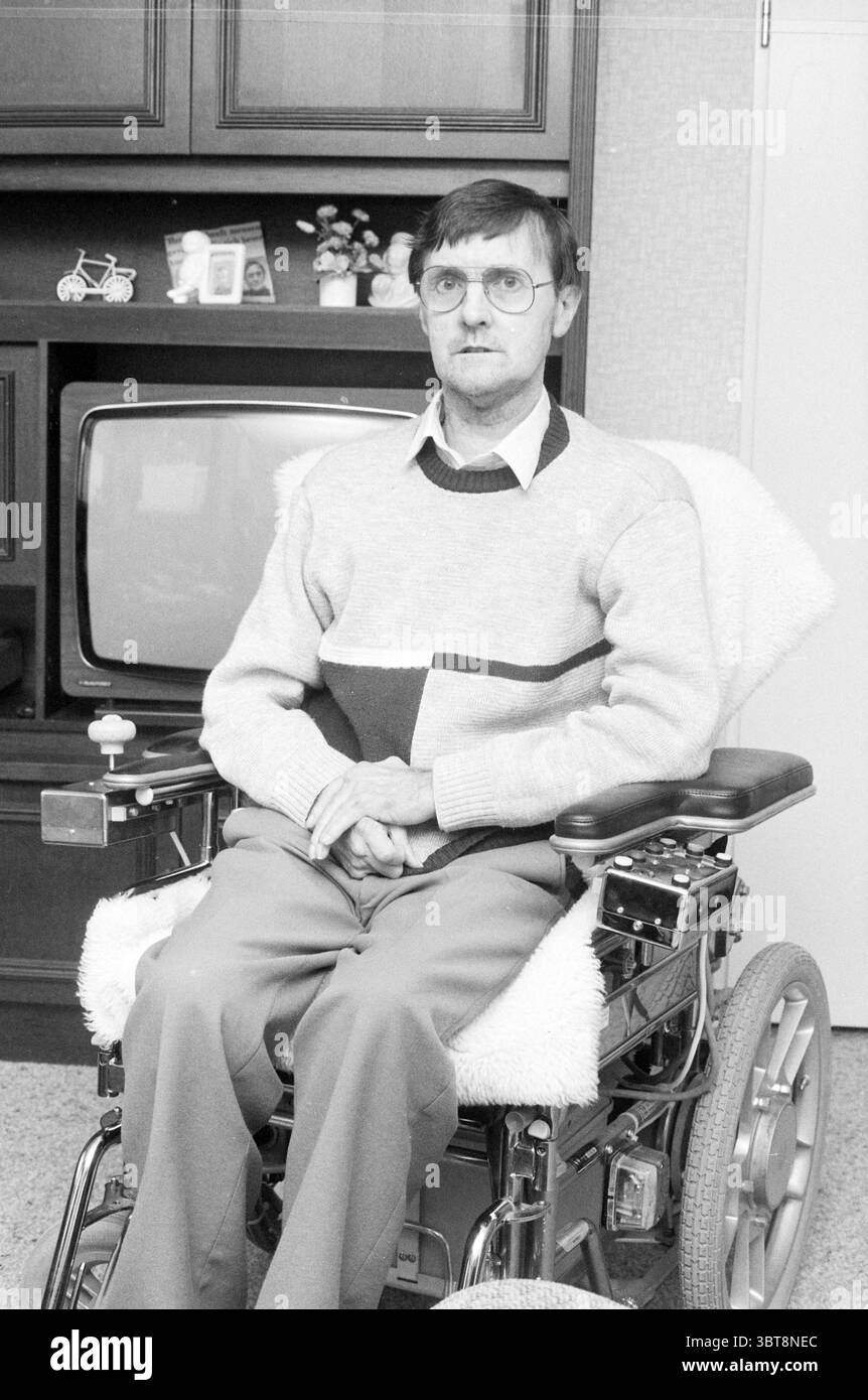 Mr. de Boer handicapé Conseiller CDA Heerhugowaard C.D.A. Heerhugowaard, Whizgle News, Dutch Desk, pays-Bas, 1950 - 2000 on 03-12-1985. Ces rubriques apparaissent dans l'image. Dans un intérieur domestique, un homme d'âge moyen est assis dans un fauteuil roulant motorisé, positionné au centre de la composition. Il a les cheveux bruns courts et porte des lunettes, lui donnant une expression réfléchie. Ses vêtements se composent d'un pull gris clair aux formes géométriques dans des tons plus sombres, et il l'associe à un pantalon beige. L'arrière-plan comporte un meuble en bois sombre qui domine le cadre, abritant des éléments comme un petit décorativ Banque D'Images