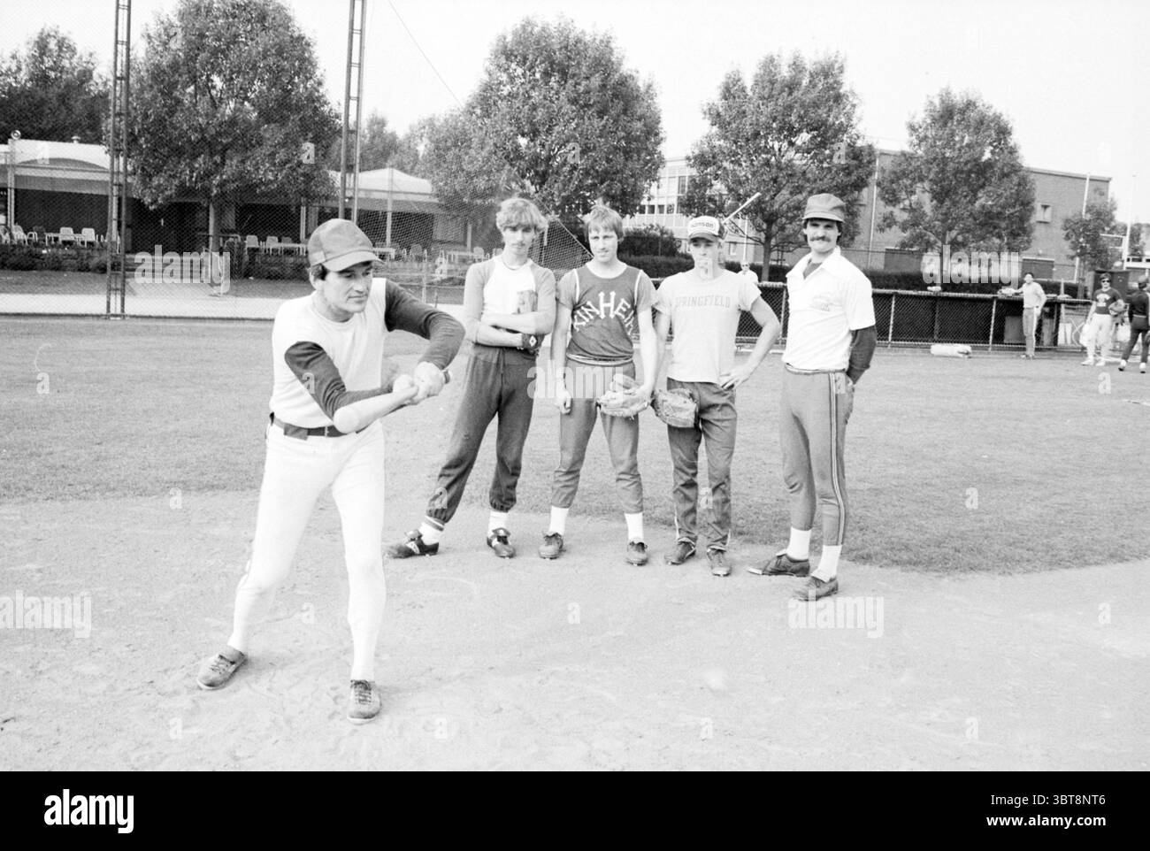 H 'ns Augustinus Baseball Kinheim, Whizgle News, Dutch Desk, pays-Bas, 1950 - 2000 le 05-07-1979. L'image inclut ces rubriques. Au premier plan, un joueur se prépare à frapper, tenant une batte de baseball avec une expression ciblée. Il est habillé d'un maillot blanc avec des manches rouges et un pantalon blanc ajusté. Sa position suggère de l'anticipation et de la préparation pour le terrain. Autour de lui se trouvent quatre autres individus, debout dans une formation détendue mais engagée. Chacun a un style distinct : l'un porte une chemise grise à manches courtes avec un logo qui jette un coup d'œil sur le bord, tandis qu'un autre Banque D'Images