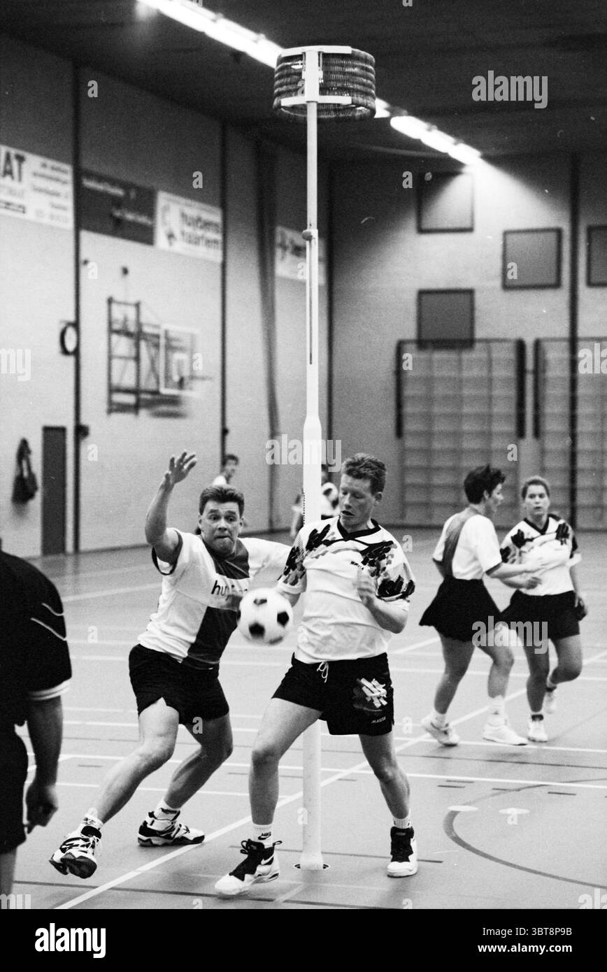 Korfball Nieuwe Flora Haarlem pays-Bas, Whizgle News, Dutch Desk, pays-Bas, 1950 - 2000 le 27-01-1996. Ces rubriques sont illustrées dans l'image. Dans une salle de sport intérieure, la scène est dynamique et énergique, avec une partie de korfball. Le cadre est spacieux, avec un plancher de salle de sport en bois et de grands murs qui reflètent l'éclairage aérien, créant une ambiance lumineuse. Un bâton blanc central avec un cerceau circulaire est fixé à une extrémité de l'aire de jeu, agissant comme cible pour marquer. Les joueurs sont engagés dans le jeu actif, avec un mélange d'expressions allant de la concentration à la détermination. Banque D'Images